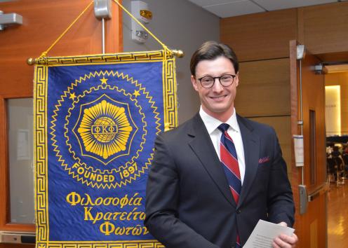 VP taking a picture in front of a Phi Kappa Phi Banner